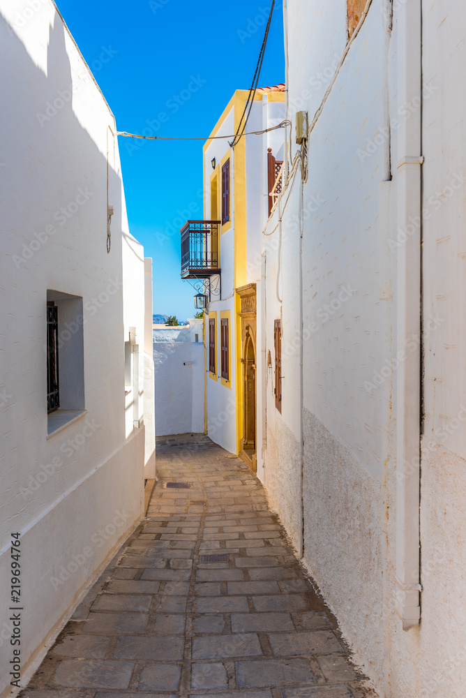 Typical Greek narrow street with white houses on Rhodes island. Lindos village, Dodecanese, Greece.
