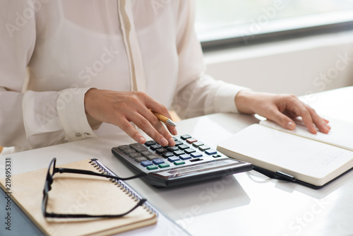 Closeup of woman calculating expenses. Notebooks, glasses and calculator lying on desk. Finance concept. Cropped view.