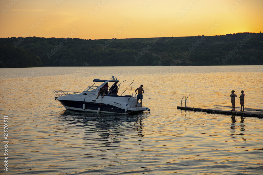 The ship is at the pier. Wives are waiting for husbands with fishing. The boat at the pier. The ship and the sunset. Orange sunset. The fishing on the ship.People on a motor boat.