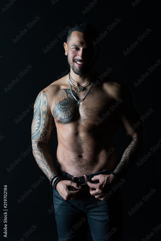 Happy man with tattoo design on skin. Bearded man shirtless with fit torso. Fashion model buckle leather belt in jeans. Sportsman smile with six pack and ab. Fitness with sport and bodycare Happy man with tattoo design on skin. Bearded man shirtless with fit torso. Fashion model buckle leather belt in jeans. Sportsman smile with six pack and ab. Fitness with sport and bodycare