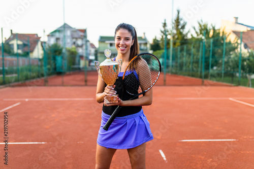 Portrait of beautiful teenage tennis player holding big trophy and smiling.