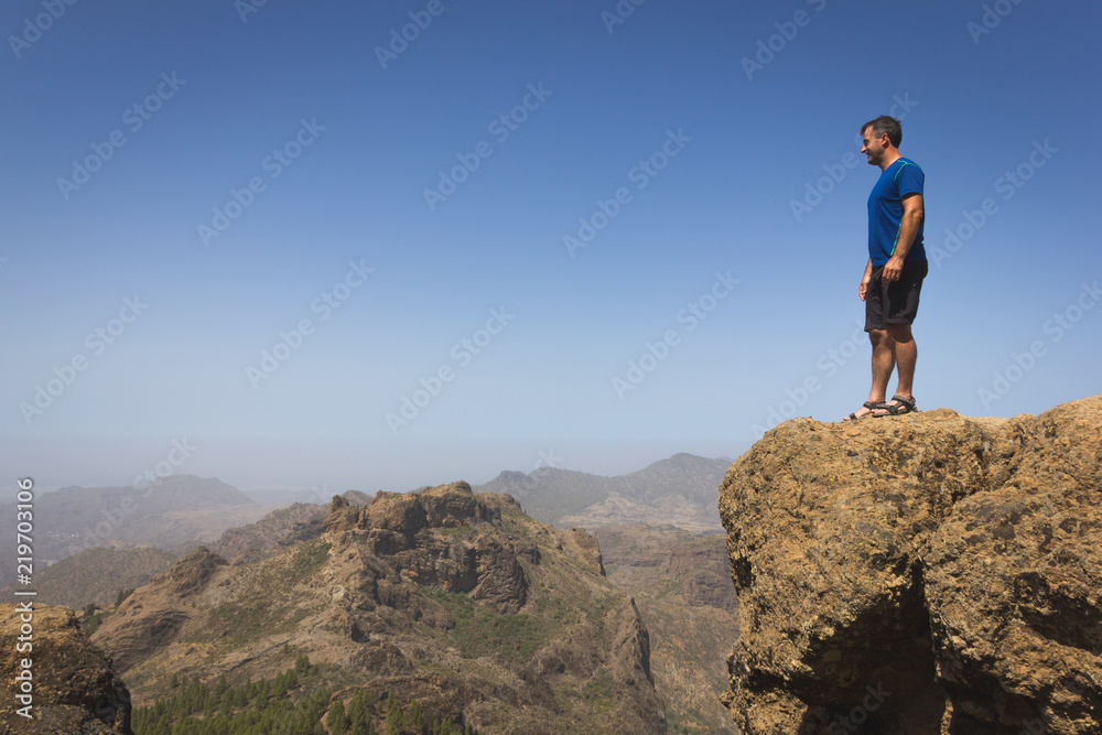 Fearless hiker looking at horizon from top of cliff edge in Roque Nublo, Gran Canaria. Adventurer on rocky mountain contemplating panoramic views. Outdoor activity, no fear, vertigo, freedom concepts