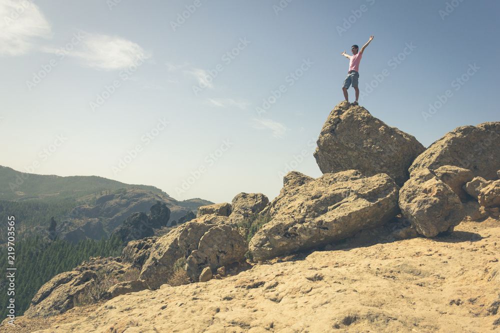 Young man standing on rock top with open arms on sunny day in Roque Nublo, Gran Canaria. Happy hiker after climbing mountain in Canary Islands, Spain. Successful, freedom concepts. Vintage effect