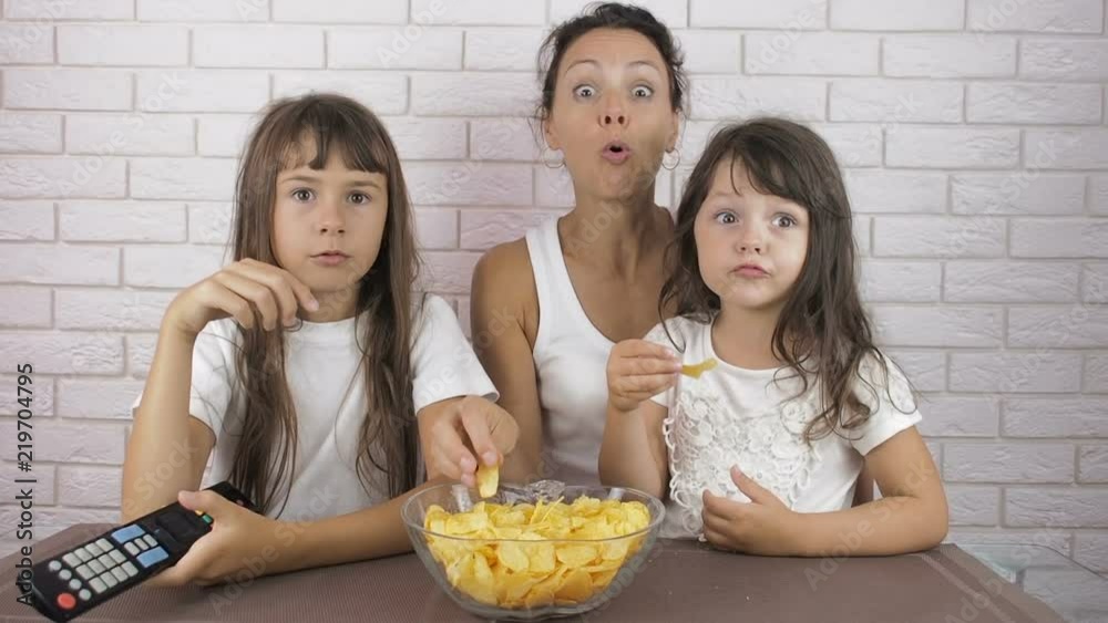 Family with harmful food. A woman with children eating chips and watching TV. Family with harmful food. A woman with children eating chips and watching TV.