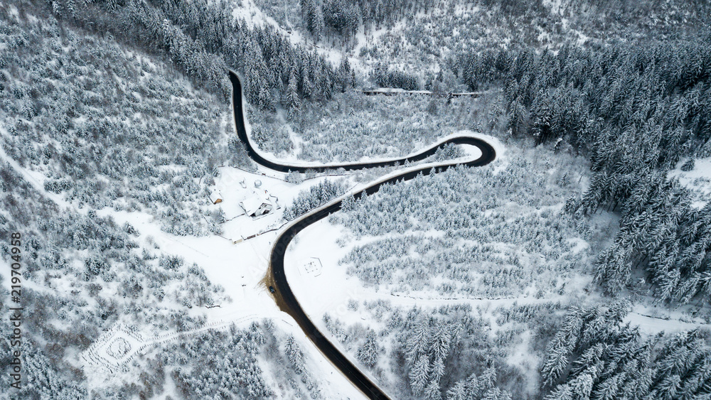 Aerial view of a road crossing through a frozen forest during a cold winter day in Romania