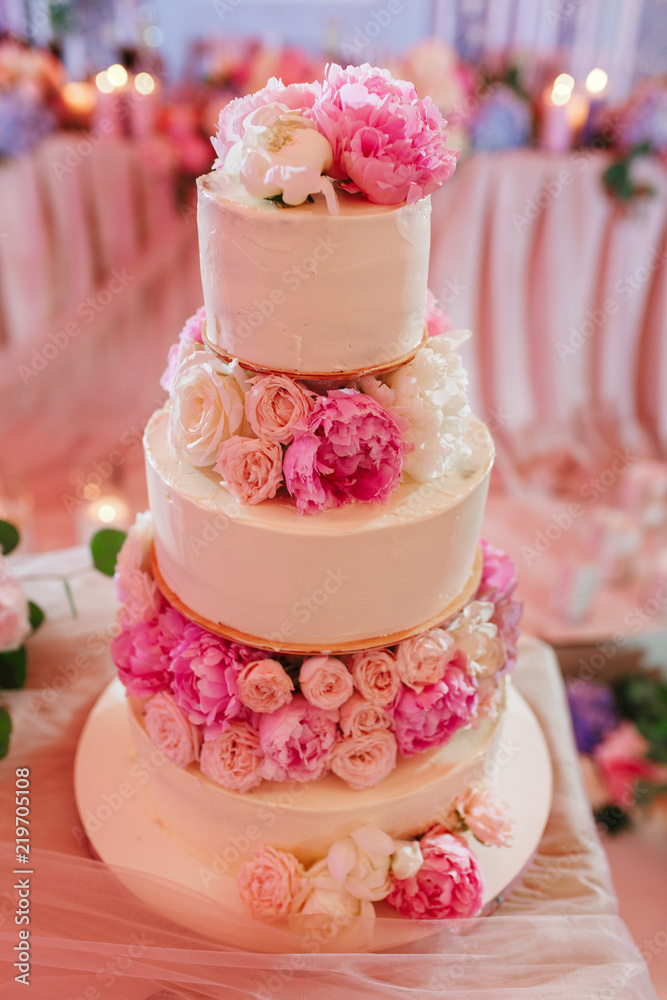 White wedding cake decorated with peony roses on pink restaurant background