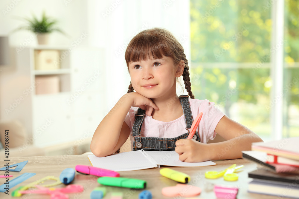 Cute girl doing homework at table with school stationery indoors Cute girl doing homework at table with school stationery indoors