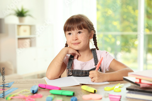 Cute girl doing homework at table with school stationery indoors