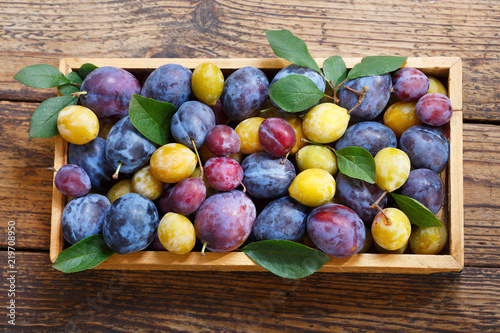 colorful plums with leaves in a wooden box