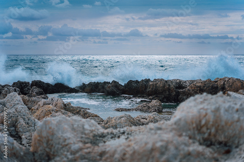Waves splashing against rocky coastline and building natural pools. Dramatic cloudscape