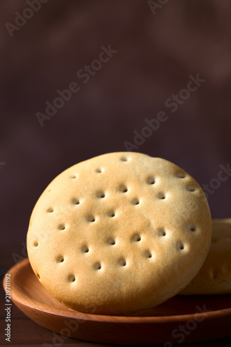 Traditional Chilean Hallulla bread roll on wooden plate, photographed with natural light (Selective Focus, Focus through the middle of the roll) photo