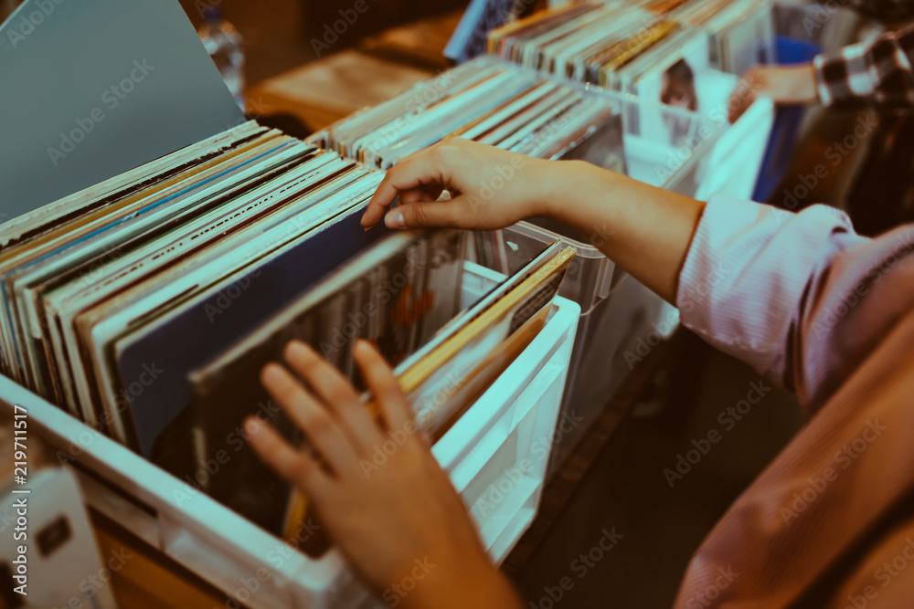 Woman is choosing a vinyl record in a musical store - obrazy, fototapety, plakaty 