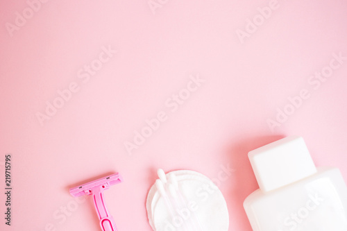 top view personal care products. white bottle, razor, ear sticks, cotton pads, toothbrush on pink background. copy space