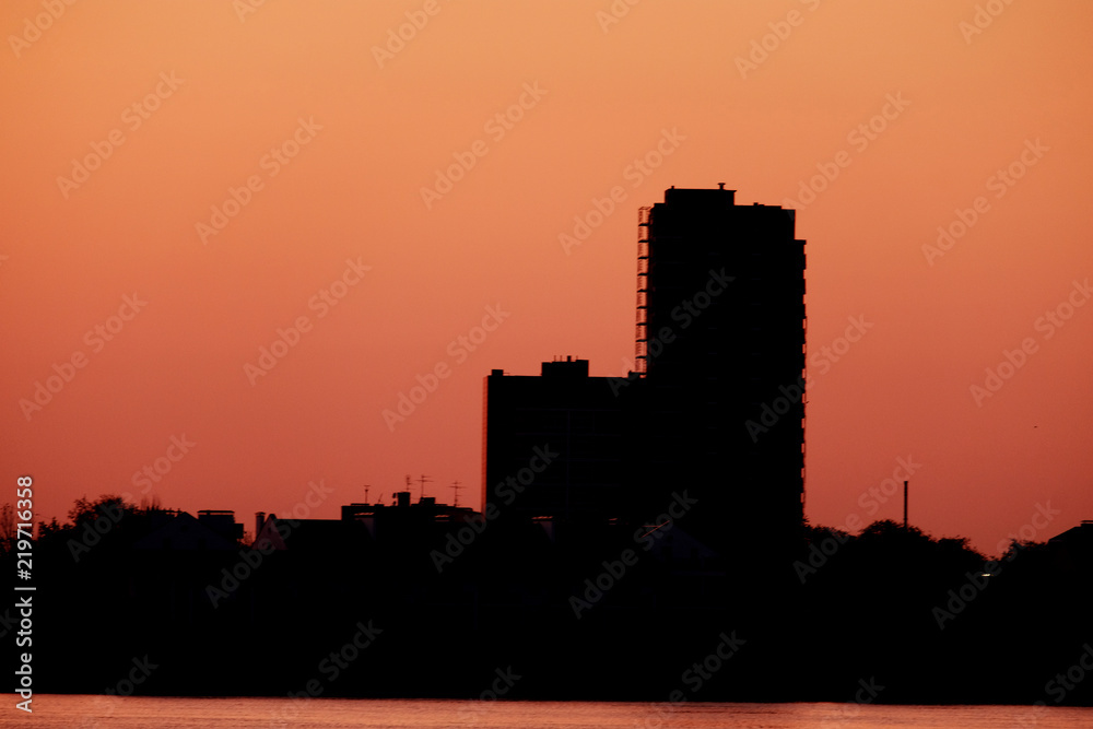 Silhouette of two tall building on waterfront in front of sunset sky