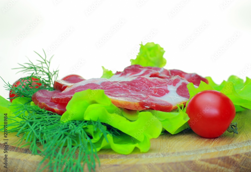 On a wooden Board is smoked bacon with vegetables. Tomato, cucumber, salad, sliced bacon are appetizing on a wooden Board on a white background