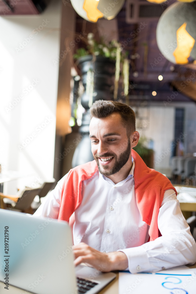 Fototapeta premium Portrait of smiling young entrepreneur using laptop while working in cafe, copy space
