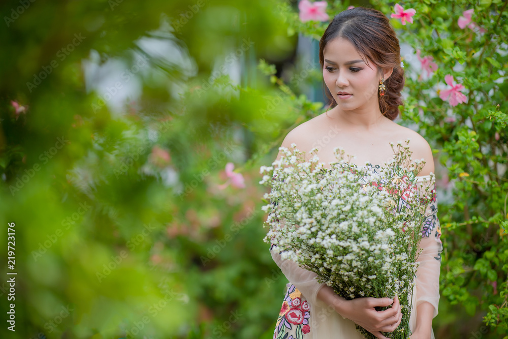 Beautiful asian bride with wedding bouquet of flowers outdoors in green park. Woman holding flower in hand over park background. Beautiful asian bride with wedding bouquet of flowers outdoors in green park. Woman holding flower in hand over park background.
