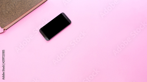 smartphone with a notebook on pink background.Top view