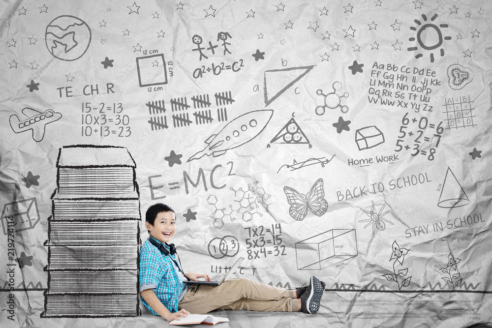 Happy schoolboy is doing schoolwork near books