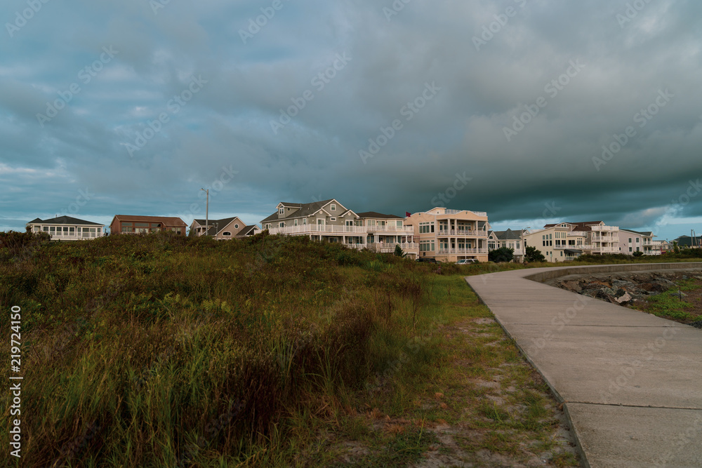 Seawall Path and Dune Grass On Dark Cloudy Beach day with Beach Homes in Background Seawall Path and Dune Grass On Dark Cloudy Beach day with Beach Homes in Background