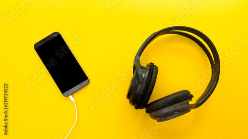 Headphones connected to smartphone over yellow background
