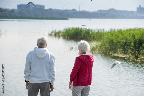 Canvas Print Rear view portrait of active senior couple standing by lake watching birds toget
