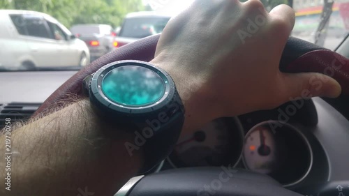 Trees are reflected in the men's watches that are clothed on the arm that keeps the car's
