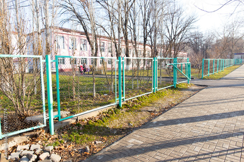 a bright cool day in the city, a wide sidewalk along the road and a green metal fence