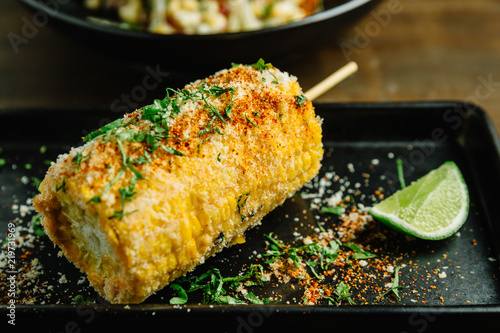 Mexican style grilled corn topping with cheese and chili powder served with sliced lime in black plate.  photo