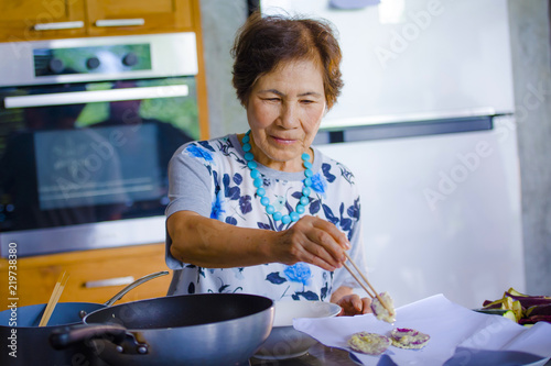 lifestyle portrait of senior happy and sweet Asian Japanese retired, woman cooking at home kitchen alone neat and tidy enjoying preparing meal photo