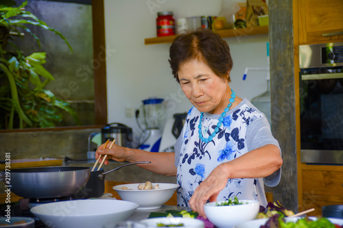 lifestyle portrait of senior happy and sweet Asian Japanese retired, woman cooking at home kitchen alone neat and tidy enjoying preparing meal