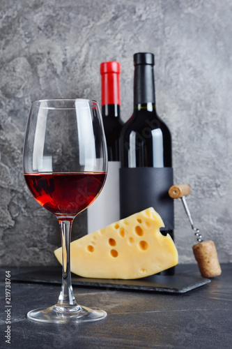 Red wine bottles with glass and cheese for tasting in cellar