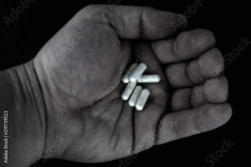 Handful of pills in hand on a dark background.