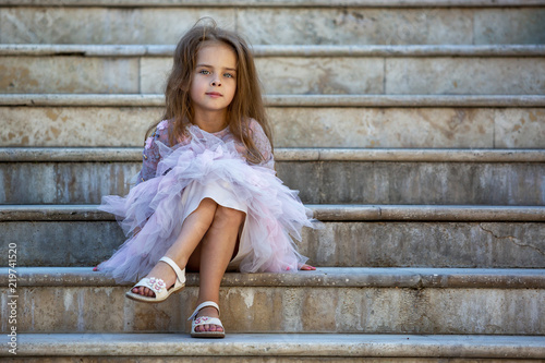 Portrait of a beautiful little girl. The child is sitting on the steps