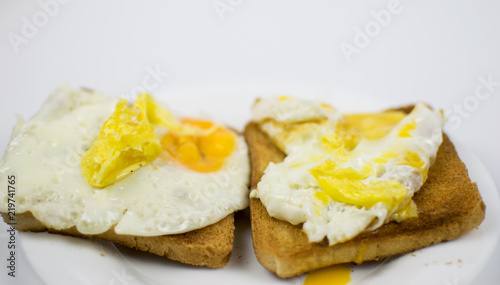 Fried chicken eggs with a burst yolk on toast on a white plate.
