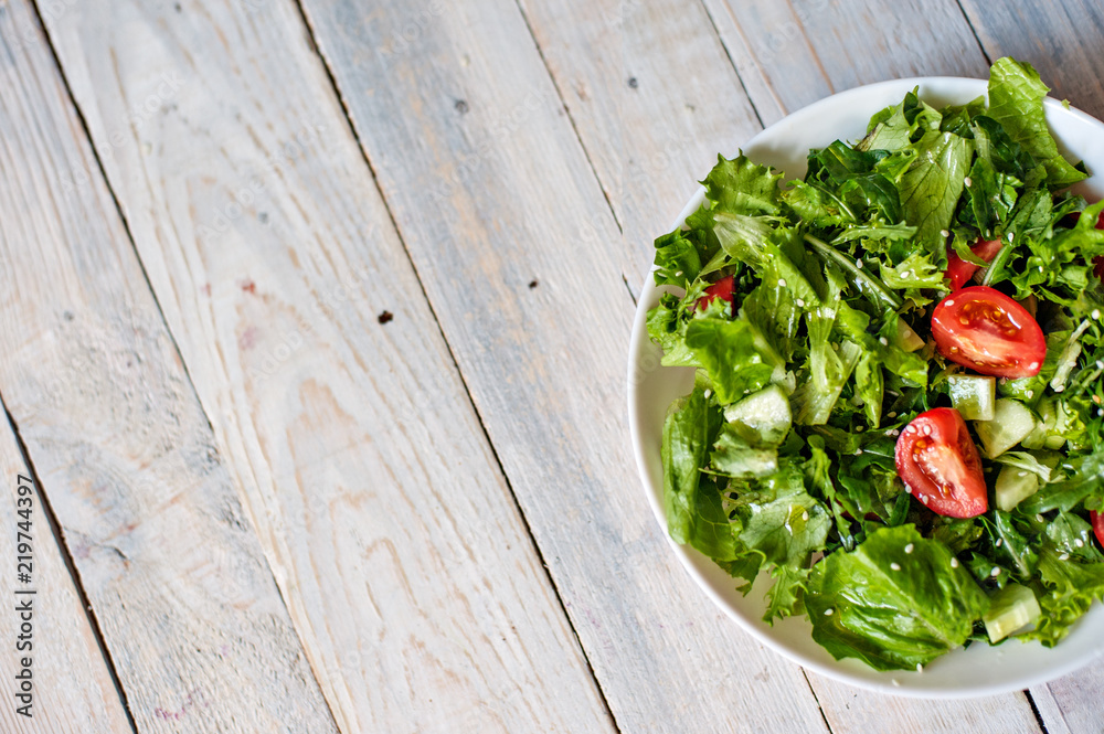 Salad from tomato, cucumbers, lettuce leaves and seeds of sesame on a white plate on a wooden background Salad from tomato, cucumbers, lettuce leaves and seeds of sesame on a white plate on a wooden background