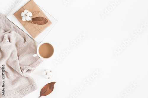 Autumn or winter composition. Cup of coffee, gift, dried autumn leaves, beige sweater on white background. Flat lay, top view, copy space