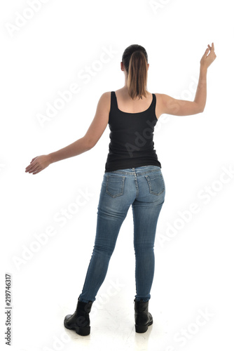full length portrait of brunette girl wearing black single and jeans. standing pose with back to the camera. isolated on white studio background. © faestock