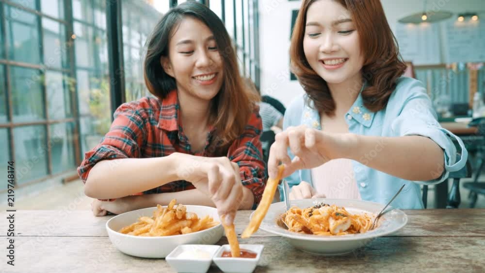 Beautiful happy Asian women lesbian lgbt couple sitting each side eating a plate of Italian seafood spaghetti and french fries at restaurant or cafe while smiling and looking at food. Beautiful happy Asian women lesbian lgbt couple sitting each side eating a plate of Italian seafood spaghetti and french fries at restaurant or cafe while smiling and looking at food.