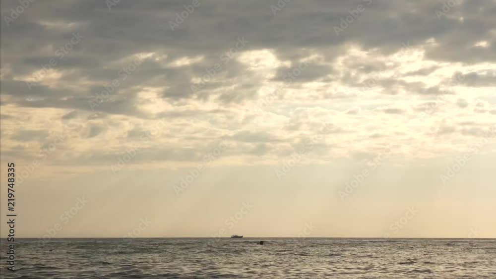 Sunset on the sea. Sun shining throw light clouds, sunbeams in the sky. Small ship moving at the horizon. Summer evening. Beautiful natural landscape Sunset on the sea. Sun shining throw light clouds, sunbeams in the sky. Small ship moving at the horizon. Summer evening. Beautiful natural landscape
