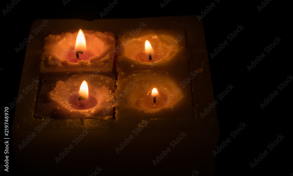 Four burning candles on a dark background.