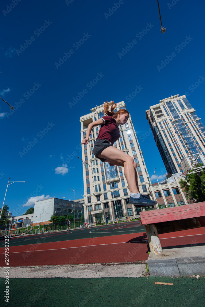 the red-haired student in shorts gives the standards for jumping at the physical education class on an open sports ground. girl doing crossfit exercises outdoor. red-haired young woman is jumping