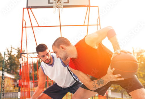 Two young friends playing basketball on court outdoors.