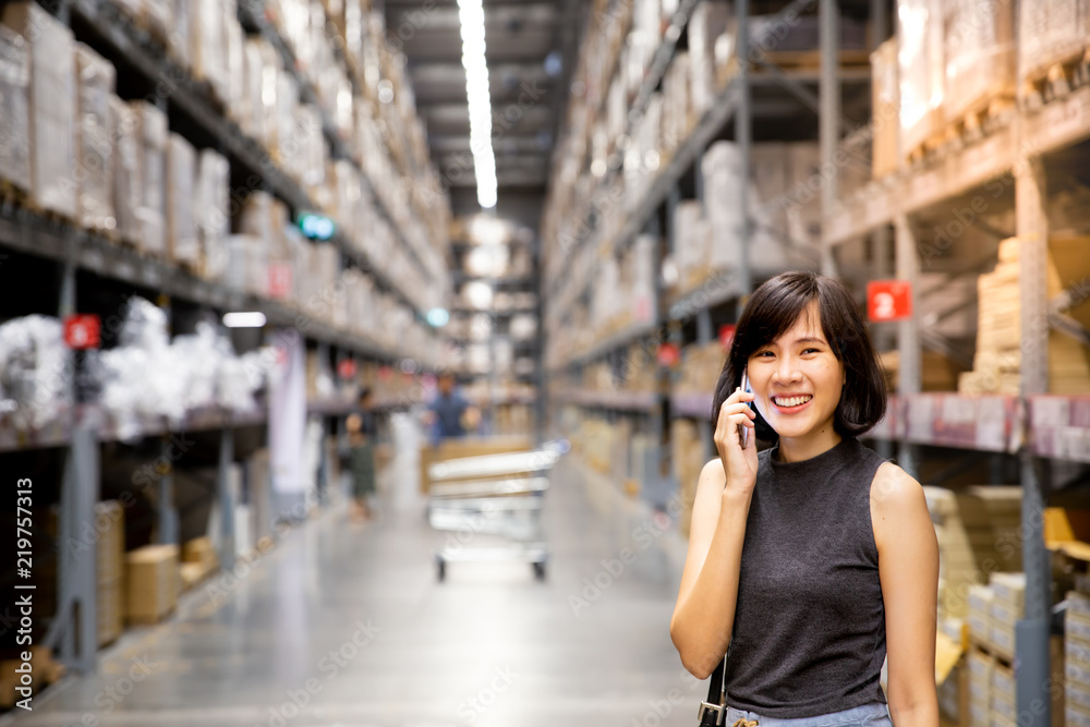An asian woman doing shopping online via mobile phone in the warehouse or mall.