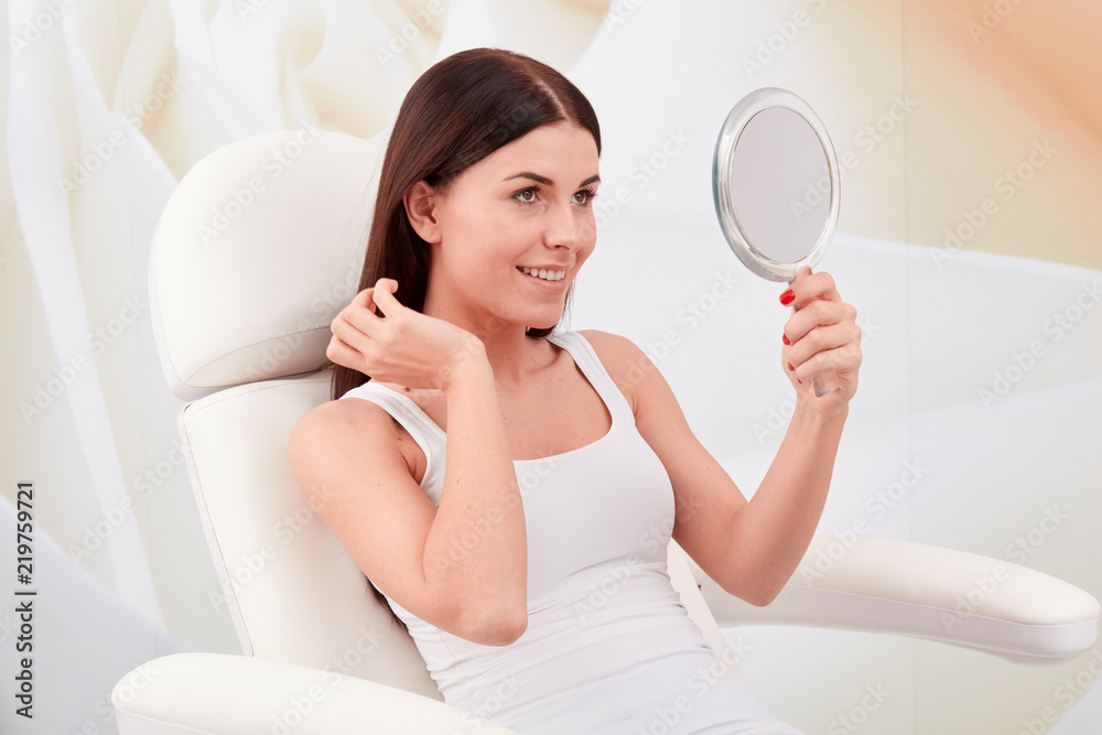 Cosmetic treatments in a professional cosmetic clinic - a young woman looks at her face in the mirror Cosmetic treatments in a professional cosmetic clinic - a young woman looks at her face in the mirror