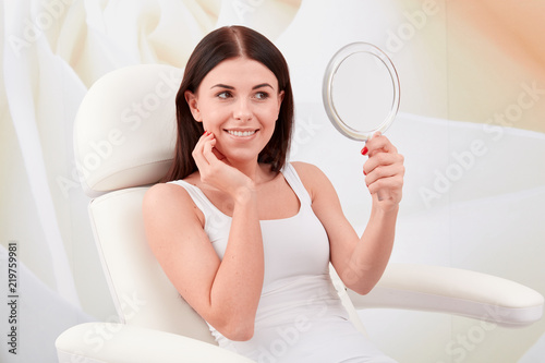 Cosmetic treatments in a professional cosmetic clinic - a young woman looks at her face in the mirror