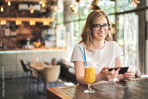 Woman texting and listening music on the mobile phone in the cafe