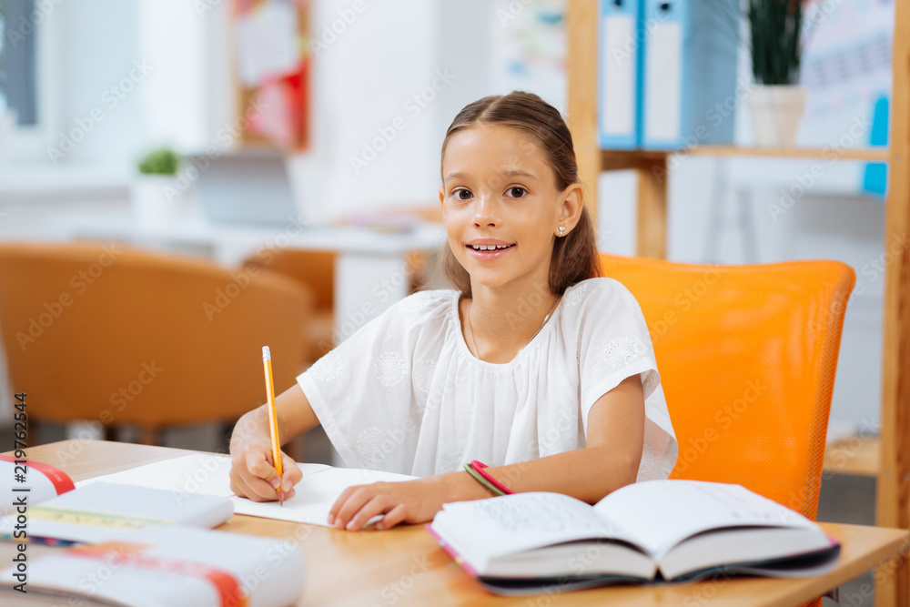 Task. Joyful cute schoolgirl sitting in a room while doing exercises Task. Joyful cute schoolgirl sitting in a room while doing exercises