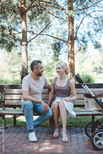 parents sitting on bench near baby carriage in park and looking at each other © LIGHTFIELD STUDIOS