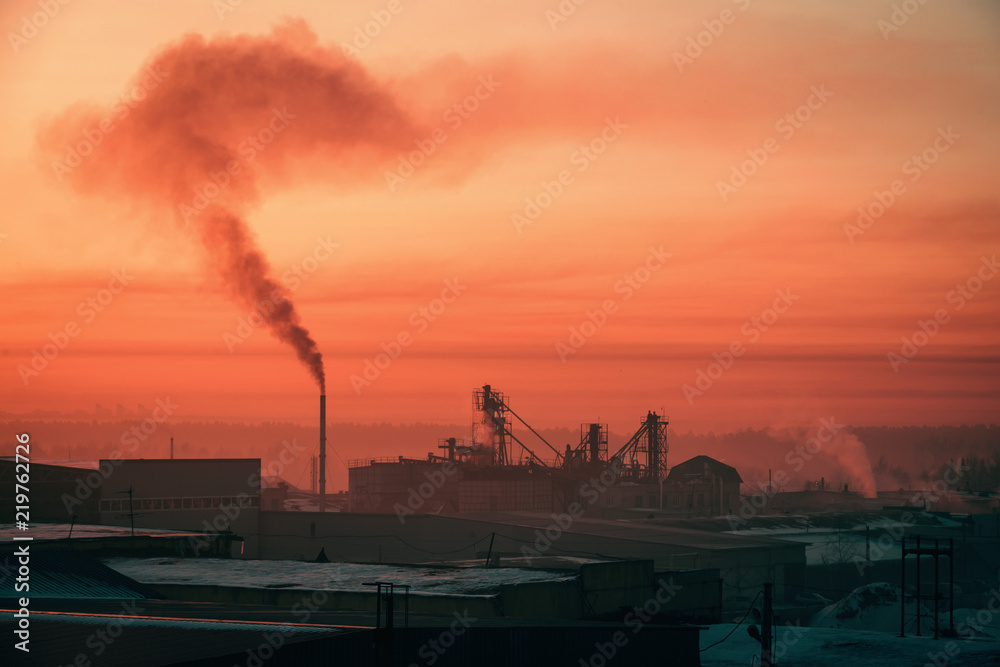Smoke from pipe pollutes environment in dawn. Storage of goods in warehouses in winter. View from above of industrial area in sunrise in pink tones. Industrial buildings zone close up with copy space.